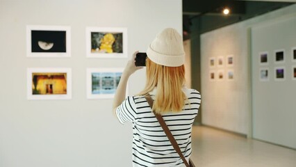 Visitor person walk looking to picture at photo frame at interior show exhibition artwork gallery, Asian woman walking through art gallery collection in front framed paintings pictures on white wall