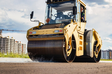 Vibratory road roller lays asphalt on a new road under construction. Close-up of the work of road machinery. Construction work on the construction of urban highways.