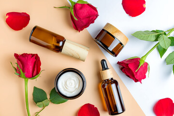 Obraz na płótnie Canvas Set of skin care products in dark glass botlles - cream, serum, fluid, mask on beige background with red roses. Unbranded mockup