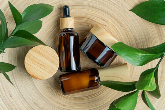 Cosmetics packaging. Set of different cosmetic bottles of cream or serum on a bamboo tray with green ruskus branches. Blank packaging. Natural beauty spa product concept. Beauty.Mock-up