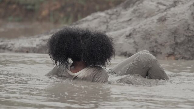 Happy child girl laying and playing in large wet mud and dirt on summer day
