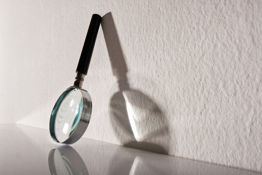 magnifying glass lean against white wall with shadow