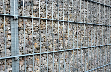 wire gabion mesh fencing and even finer mesh holding the pebbles sprinkled inside between. visual full anti-noise material around the road, breaks the traffic noise from the street