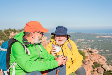 Obraz na płótnie Canvas Two happy elderly trekkers sitting on the summit with a cup