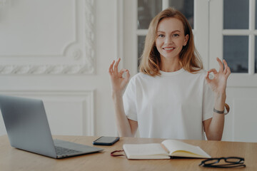 Female keep calmness practicing yoga at office desk at laptop on workplace. Anti-stress break