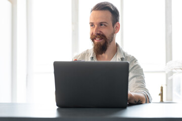 Stylish bearded man working on laptop from home sitting at the table