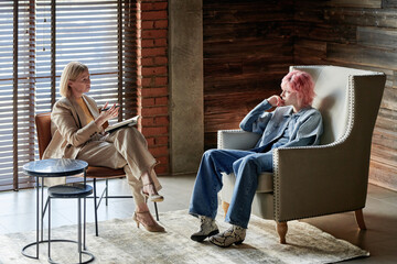 Teenager sitting on comfortable armchair and listening the advice of psychotherapist in the room