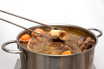 Beef Bone Broth in metal pan, close-up, selective focus. Bones contain collagen, which provides the...