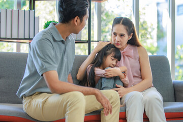 Millennial Asian unhappy family mother sitting on sofa couch holding hugging soothing little young...