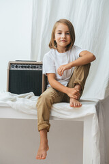 Cute tween girl sitting on a table barefoot next to a guitar amp.
