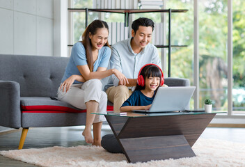 Millennial Asian happy family father and mother sit on cozy sofa couch smiling helping teaching...