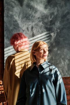 Mature woman with blond hair standing against young girl with pink hair at studio