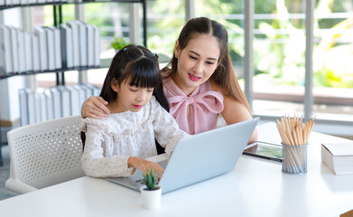 Fototapeta premium Millennial Asian happy family mother smiling helping supporting teaching little girl kid daughter studying learning doing online school homework via laptop notebook computer in living room at home