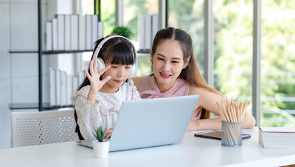 Millennial Asian happy family mother smiling helping supporting teaching little girl kid daughter studying learning doing online school homework via laptop notebook computer in living room at home