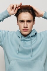 Close-up photo. a handsome young man looks into the camera in a light light blue hoodie,with a comb in his hand combing a place in the background for inserting an advertising layout.Vertical portrait