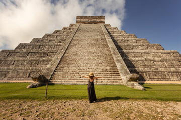 Woman wearing hat and black dress (back view, unrecognized) in front of the Chichen-Itza pyramid in...