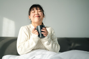 Young woman drinking coffee in bedroom, Holding coffee cup with two hands