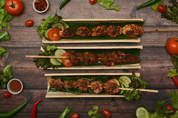 Grilled meat skewers served in bamboo barrel plate with fresh vegetable on wooden background