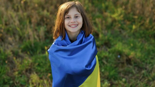 Portrait of Child with Ukrainian flag in field. Little girl waving national flag praying for peace. Happy kid celebrating Independence Day. Pray for Ukraine