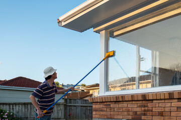 Man washing windows with long pole and brush. Home maintenance project.