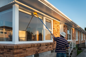 Man washing windows of an empty house with long pole and brush. Home refurbishment project in...