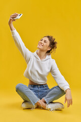 Side view of pretty model posing for photo. Beautiful girl with curly hair sitting in lotos pose,...