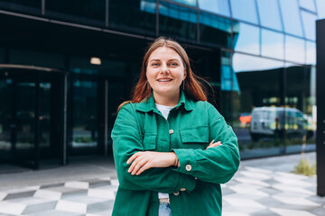 Modern business woman standing near Office Building. Crossed arms. Huge blurred office windows on the background. High Resolution photo.