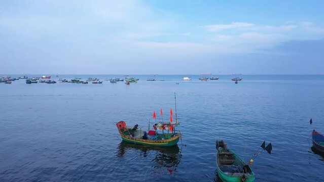 Aerial fly over a small Vietnamese fishing boat returns to shore after a night at sea. It is painted green, orange and red. Fishermen are emptying the nets. Location is Vung Tau.