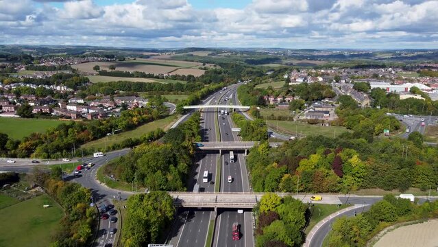 Aerial drone footage of the busy M1 motorway with three bridges crossing over the highway, filmed in the village of Barnsley in Sheffield UK in the summer time on a bright sunny summers day.