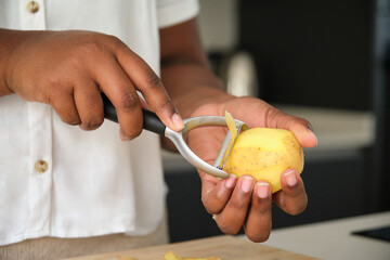 Close up of cuban woman hands peeling a raw potato using a peeler.