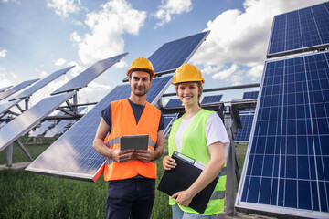 Standing in front of the camera two ecological engineers lady and man in the middle of photovoltaic...