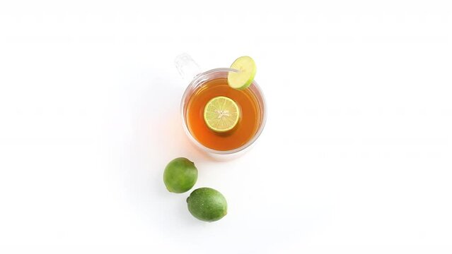 lemon tea in a transparent glass cup with whole and sliced lemon in white background rotating top shot
