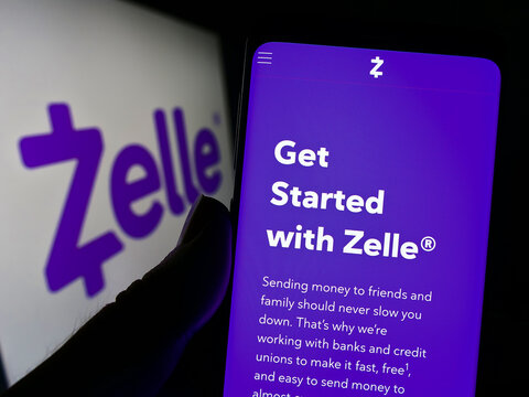 Stuttgart, Germany - 10-15-2022: Person holding cellphone with website of US digital payments company Zelle on screen in front of business logo. Focus on center of phone display.