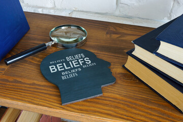 Head with words beliefs on the shelf and magnifying glass. - obrazy, fototapety, plakaty