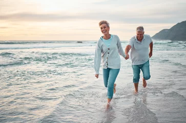 Fotobehang Beach, walking and senior couple holding hands for support, love and care with outdoor wellness, retirement and holiday lifestyle with sunset sky. Elderly people running together in sea ocean water © David Lahoud/peopleimages.com