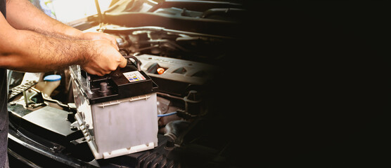 A auto mechanic carries a replacement car battery for car electrical maintenance , panoramic banner with copy space on black background