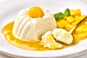 Macro spoon with piece of homemade panna cotta with natural vanilla pod, mango syrup and mint, selective focus