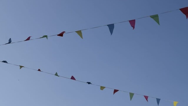 Two rows of colored bunting flutters in the wind under a clear blue sky. These remind us that it is party time in some towns during the summer