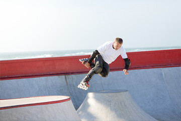 Energetic man on roller skates in motion at modern roller skate park. Roller skater doing dangerous and daring tricks. Sport, health, speed, and energy