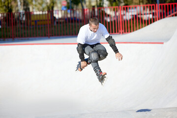 Mature male inline roller training in public skate park. Practicing jumps, tricks. Concept of...