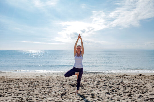 Wellness concept. Caucasian woman exercise practicing yoga on the shore looking at the camera. Outdoors sport and fitness lifestyle image.