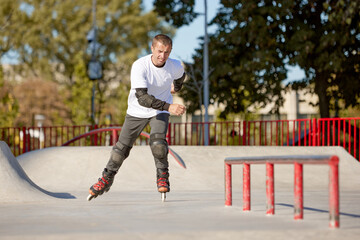 Mature male inline roller training in public skate park. Practicing jumps, tricks. Concept of...