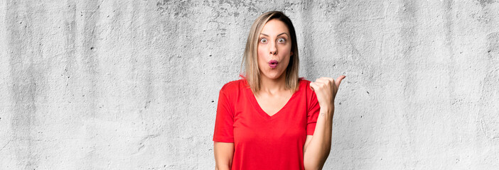 blonde adult woman looking astonished in disbelief, pointing at object on the side and saying wow,...