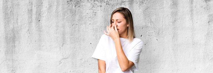 blonde adult woman feeling disgusted, holding nose to avoid smelling a foul and unpleasant stench