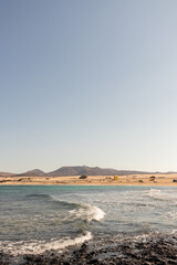 Amazing seascape of yellow sand beach and volcanic rocks with mountains in the distance.Fuerteventura, Canary Islands, Spain