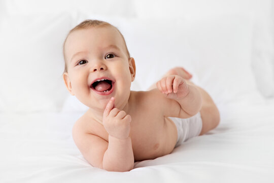 Happy baby lying on stomach on white bed with funny expression