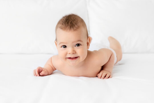 Smiling baby lying on stomach on white bed