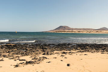 Amazing seascape of yellow sand beach and volcanic rocks with mountains in the distance.Fuerteventura, Canary Islands, Spain