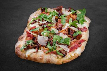 Pizza Carbonara with bacon, chanterelles, arugula, mozzarella, parmesan, pesto. Roman pizza rectangular on dark background
