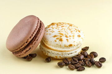 Chocolate and vanila macaroons with roasted coffee beans on yellow background
